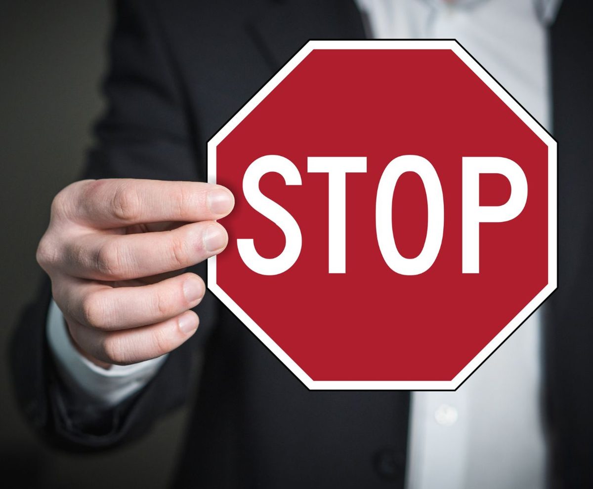 Persona con traje sosteniendo una señal de stop roja ante el rostro