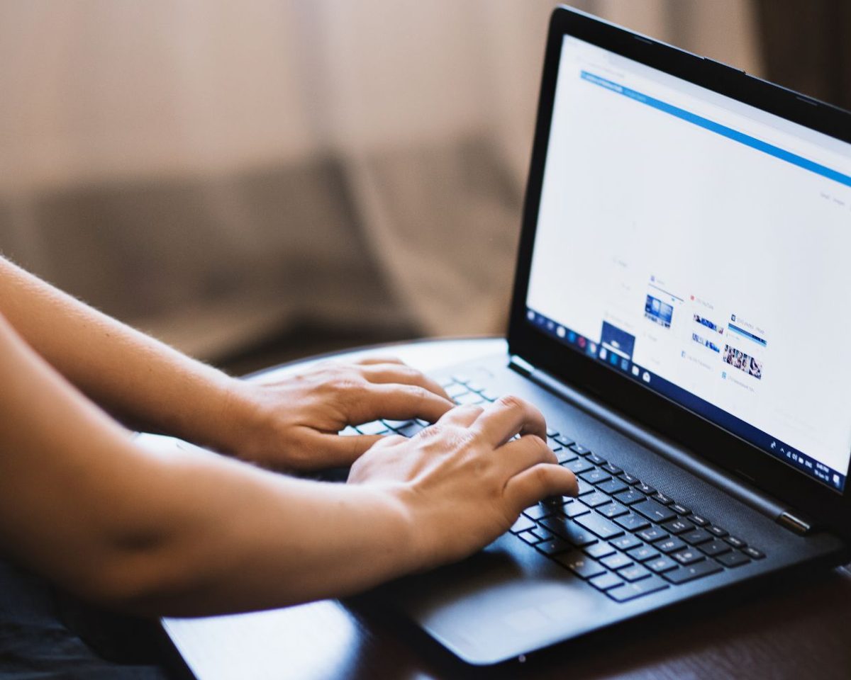 Manos tecleando en un portátil con una página web abierta en pantalla