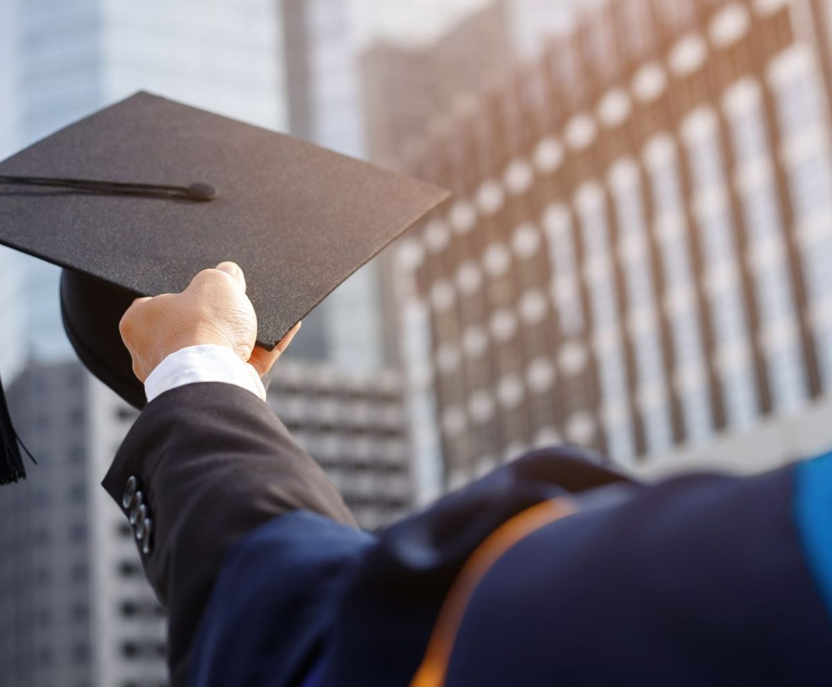 Persona sosteniendo un birrete de graduación frente a edificios de oficinas