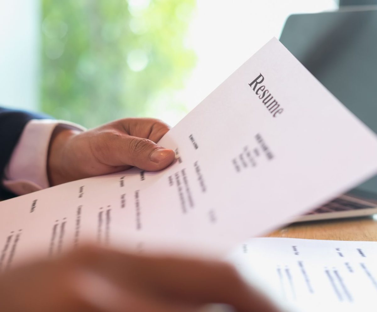 Mano sosteniendo un currículum rosa con la palabra Resume sobre una mesa de oficina