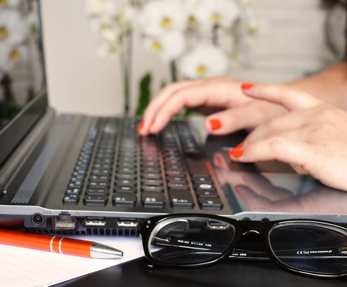 Manos escribiendo en un portátil con gafas y un bolígrafo sobre la mesa
