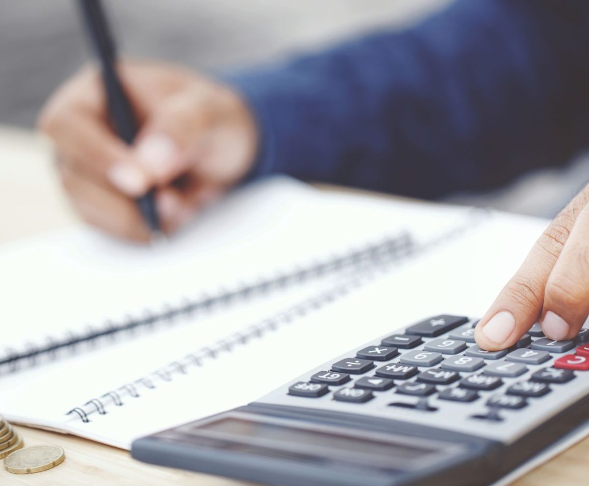 Mano con un bolígrafo sobre un cuaderno junto a una calculadora
