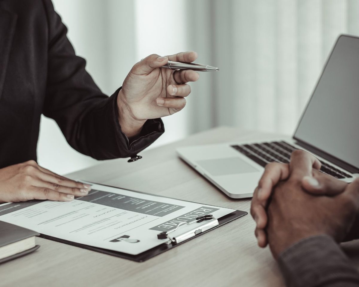 Mano con un bolígrafo sobre un documento en una mesa de oficina junto a un portátil