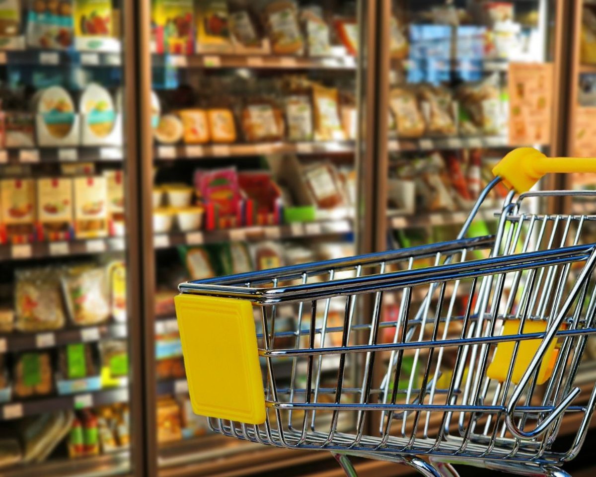 Carro de la compra amarillo frente a estanterías con productos de un supermercado