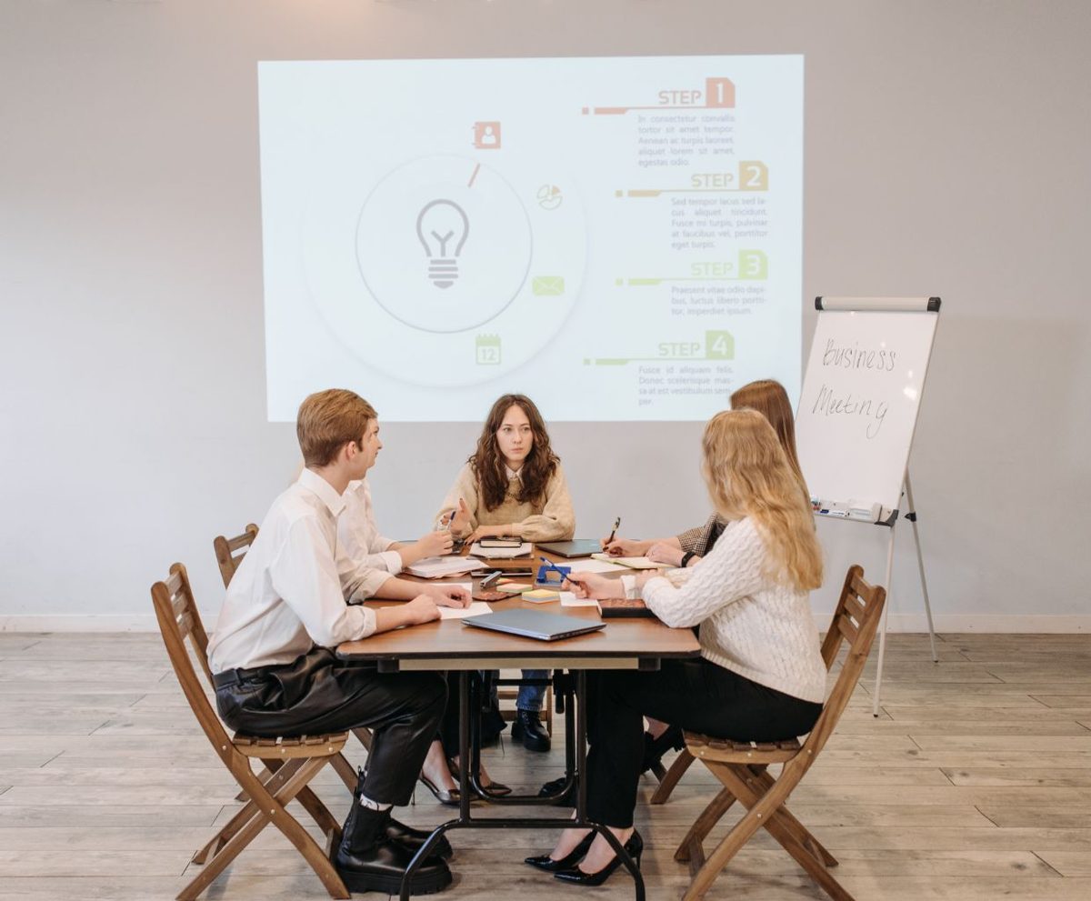 Personas sentadas alrededor de una mesa en una sala de reuniones con una pantalla al fondo