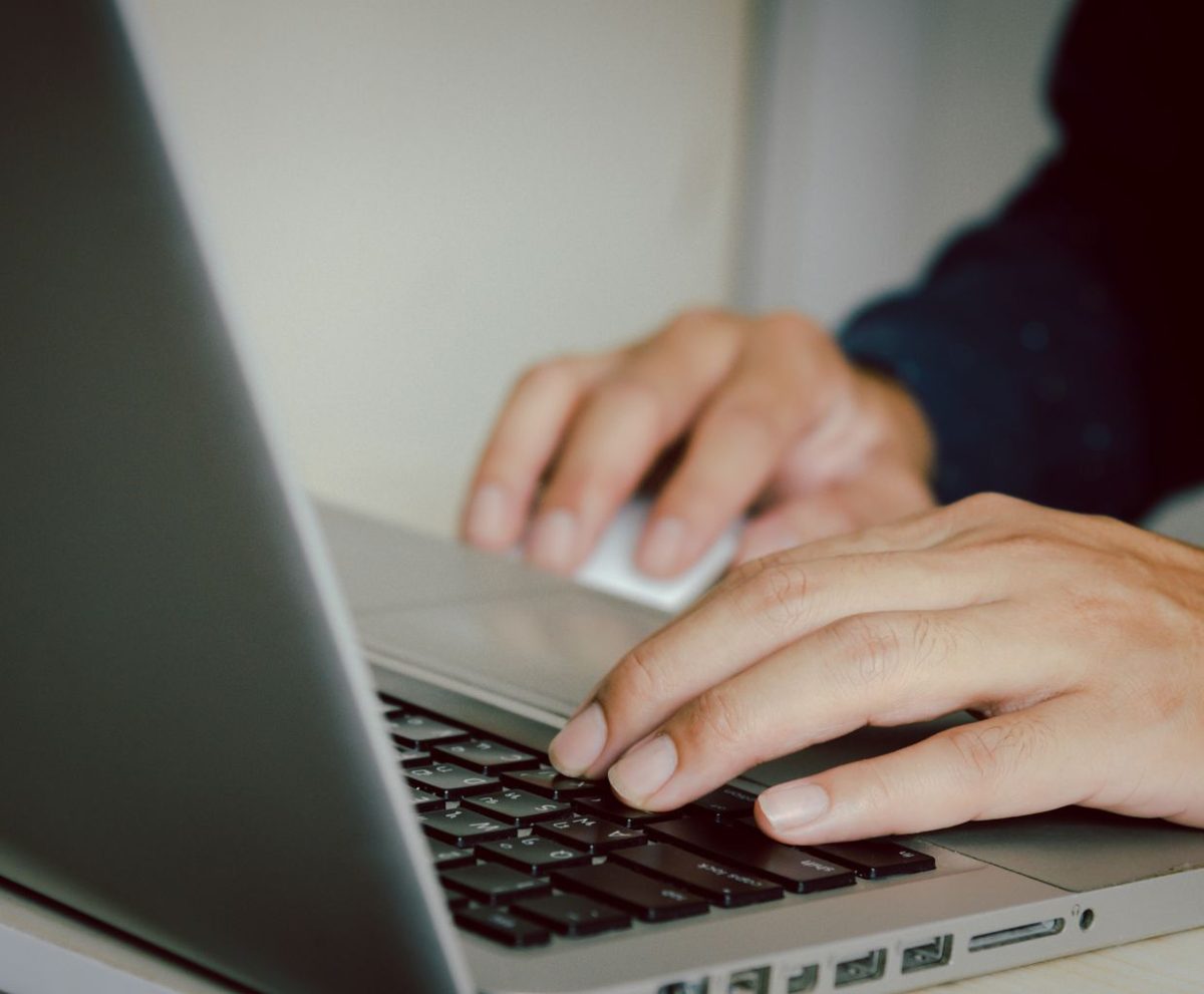 Manos escribiendo en el teclado de un portátil con la pantalla inclinada hacia la izquierda