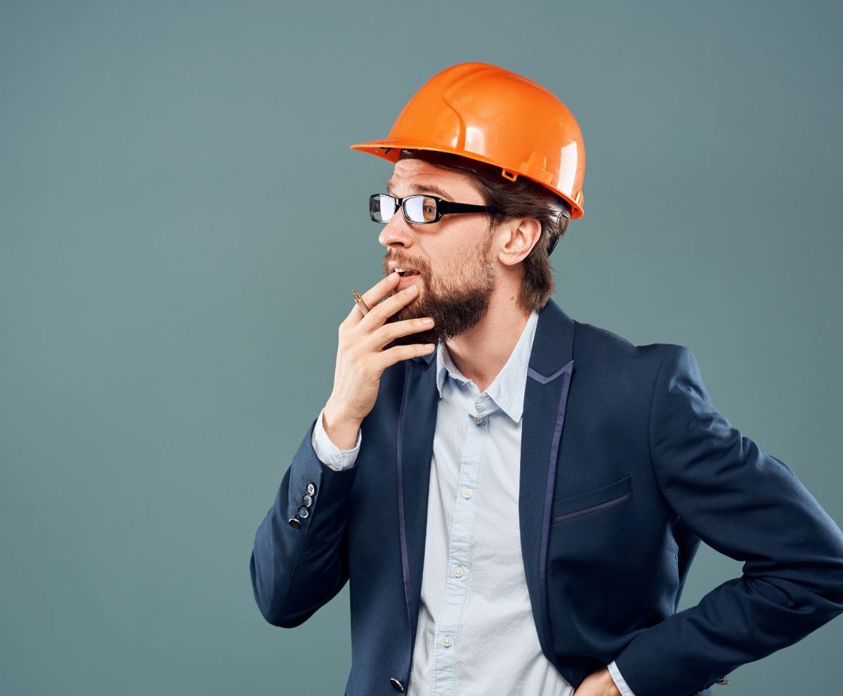 Hombre con un casco naranja y la mano en la barbilla pensando