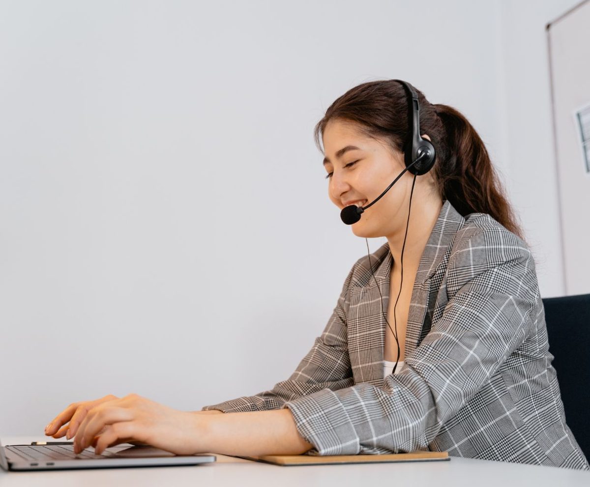 Mujer con auriculares de atención al cliente sonriendo ante un portátil