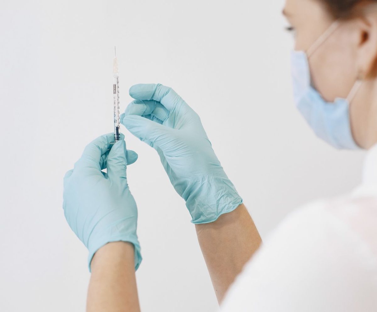 Manos con guantes sanitarios sujetando un vial y una jeringa