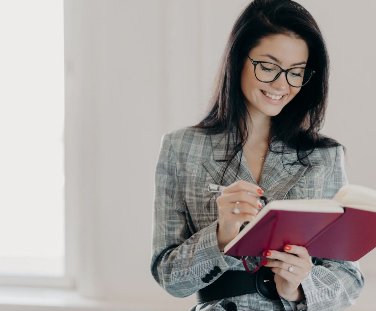 Mujer con gafas sonriendo mientras sostiene un cuaderno