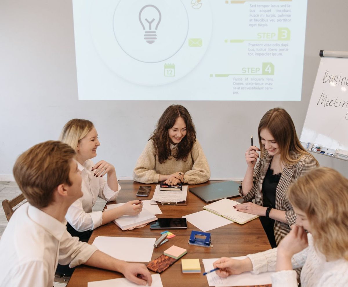 Grupo de personas trabajando en una mesa con una pantalla de proyecto al fondo