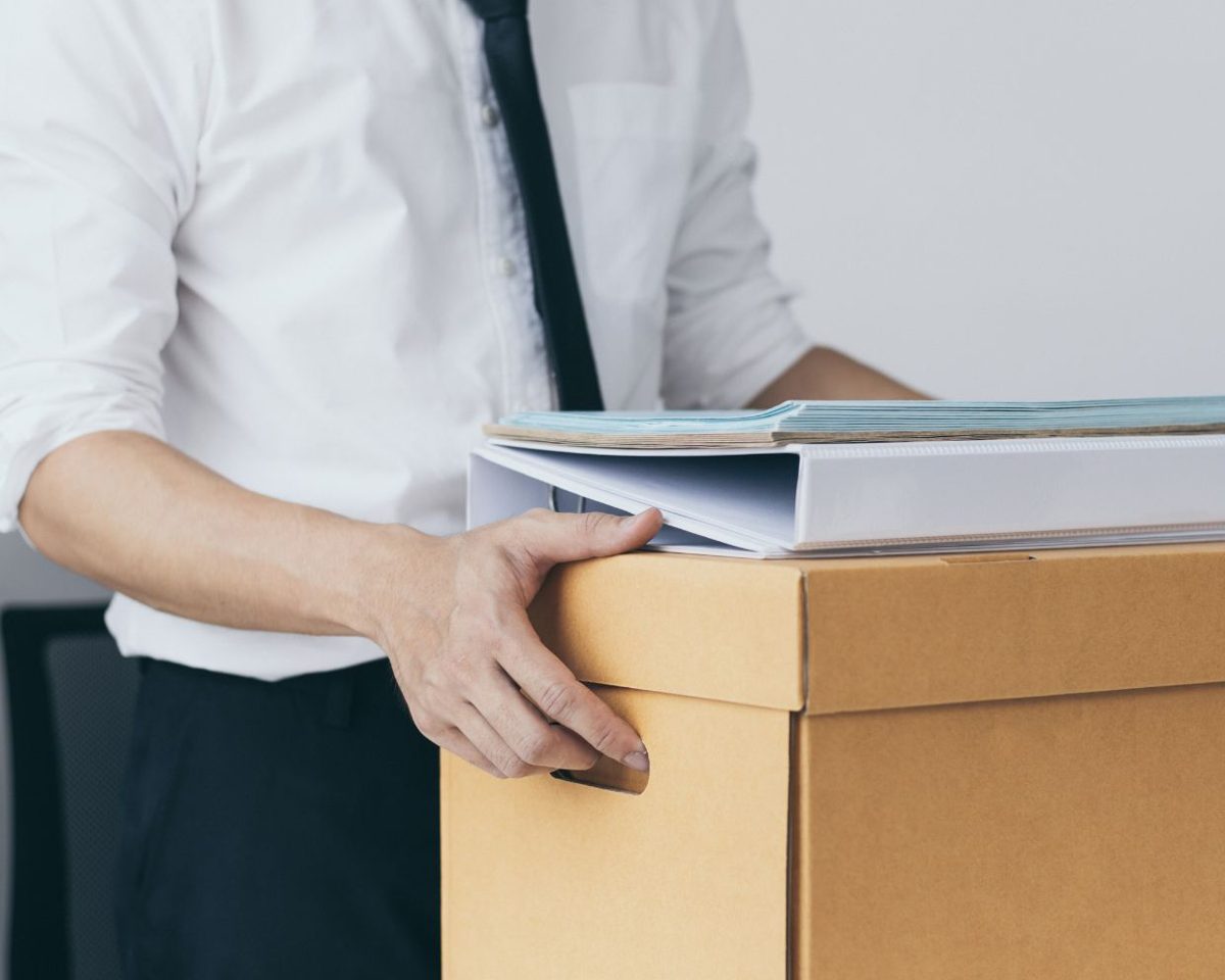 Hombre con camisa blanca y corbata sosteniendo una caja de cartón con una carpeta sobre ella