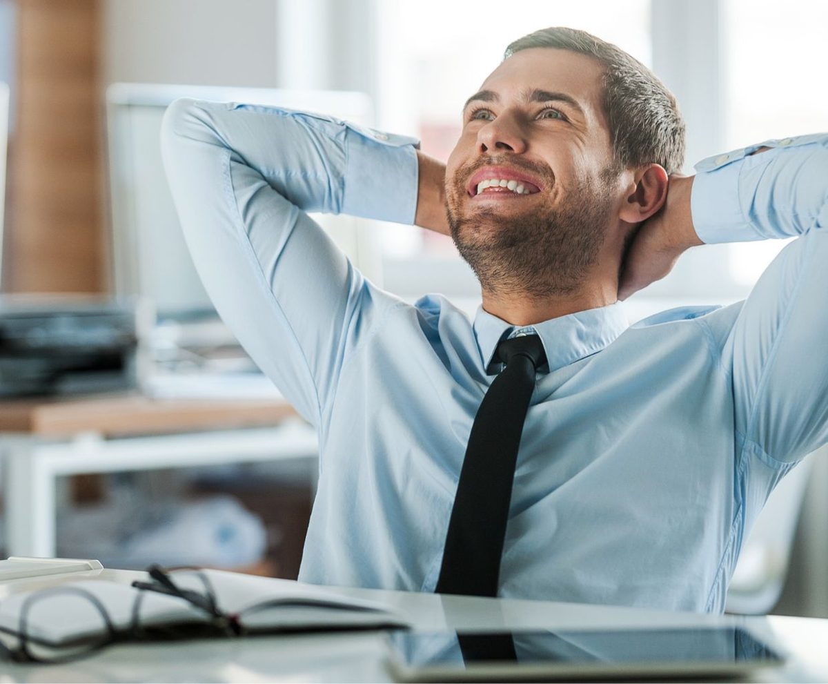 Hombre sonriente en una mesa de oficina con las manos detrás de la cabeza