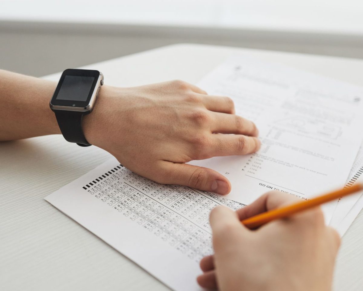 Mano con un reloj de pulsera escribiendo sobre un formulario en una mesa blanca