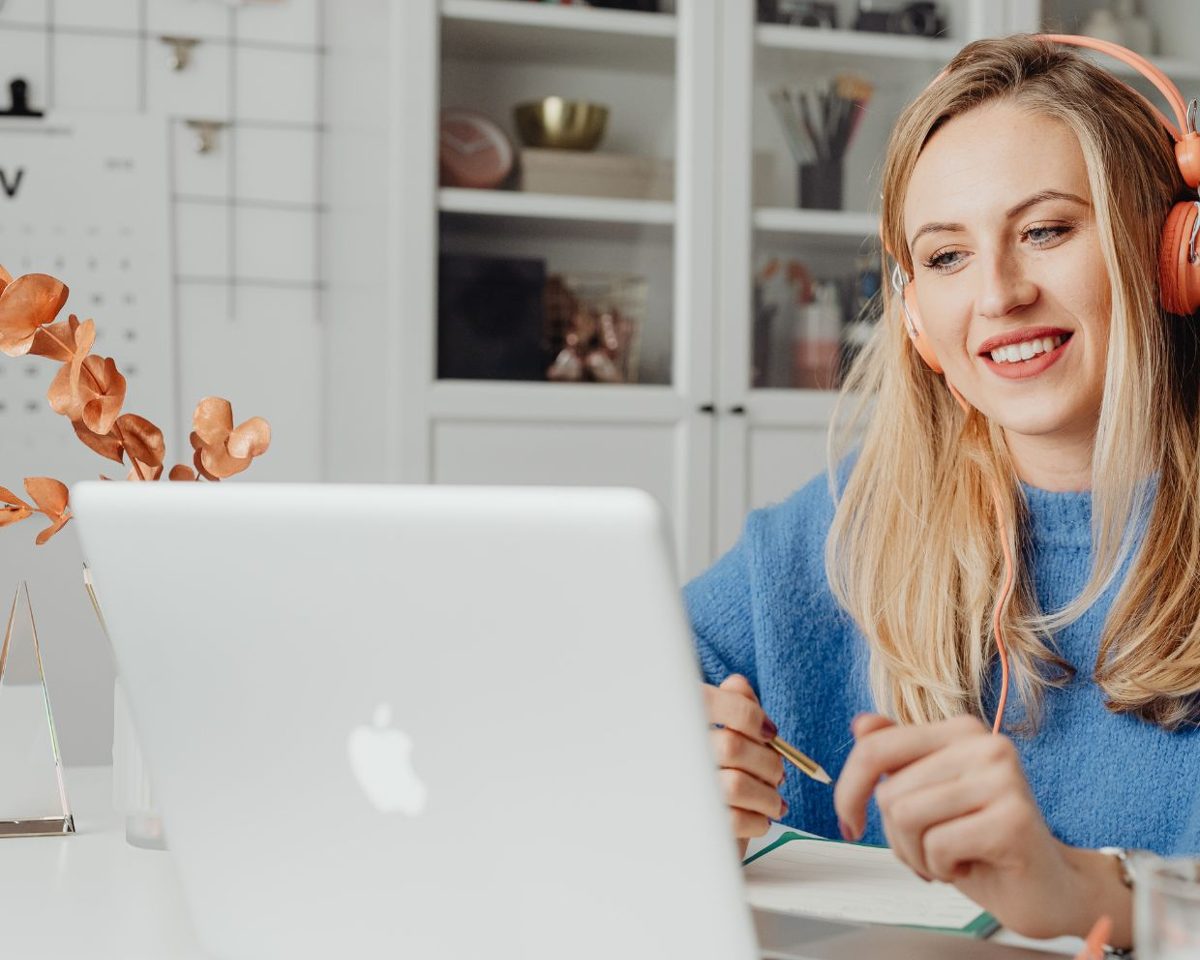 Mujer rubia sonriendo frente a su portátil en una mesa luminosa con estanterías al fondo