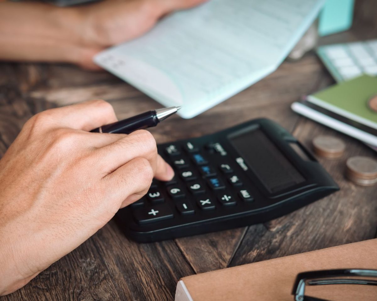 Mano usando una calculadora sobre una mesa de madera junto a un cuaderno y papeles