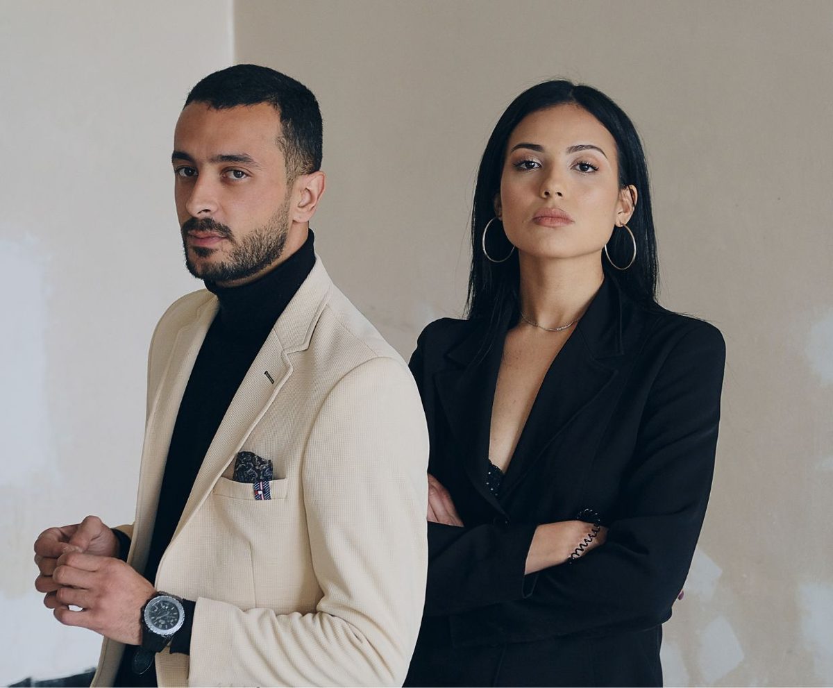 Hombre y mujer con ropa elegante posando de pie con los brazos cruzados ante un fondo neutro