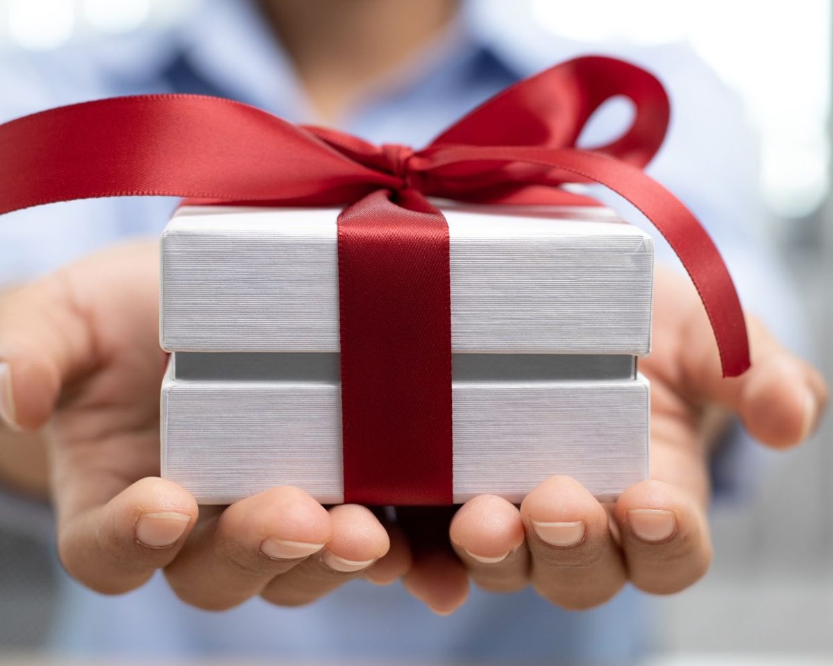 Mano sosteniendo una caja de regalo plateada con un lazo rojo