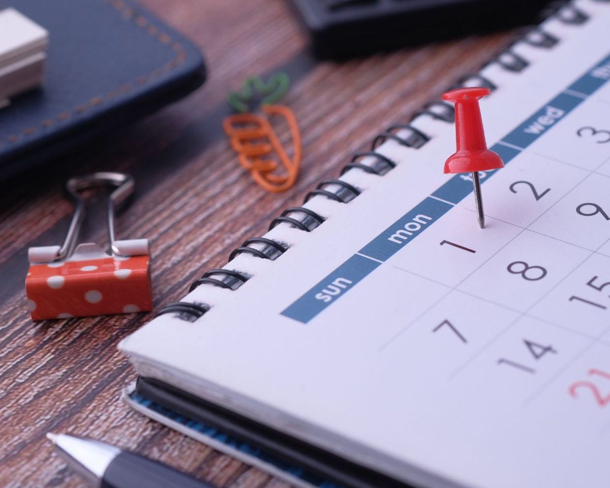 Agenda con un calendario mensual y una chincheta roja sobre una fecha marcada