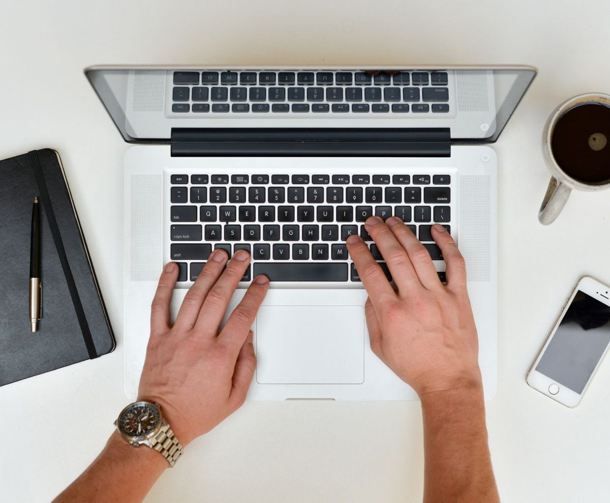 Manos escribiendo en un portátil sobre una mesa de trabajo
