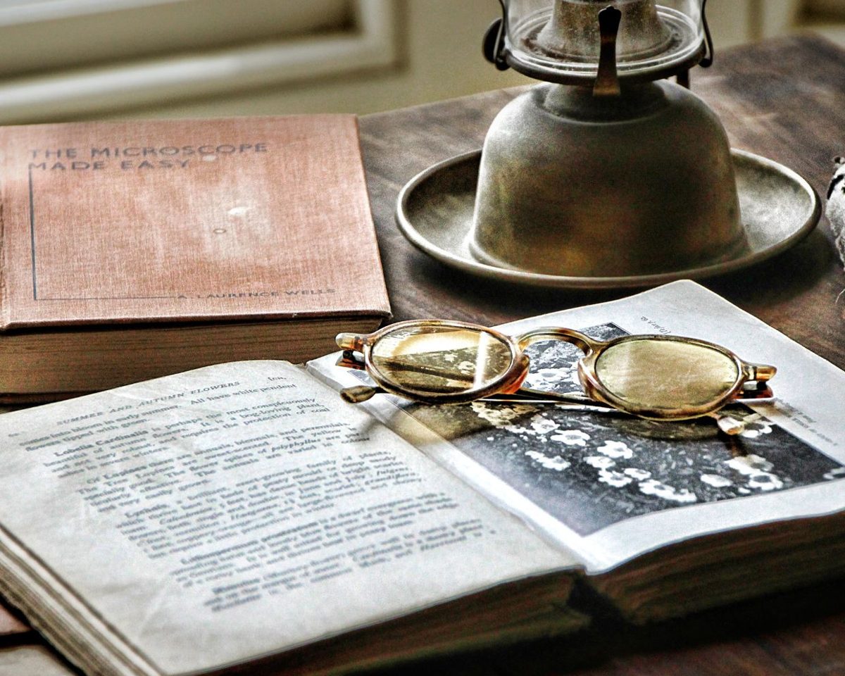Libro antiguo abierto junto a unas gafas y una lámpara de aceite sobre una mesa