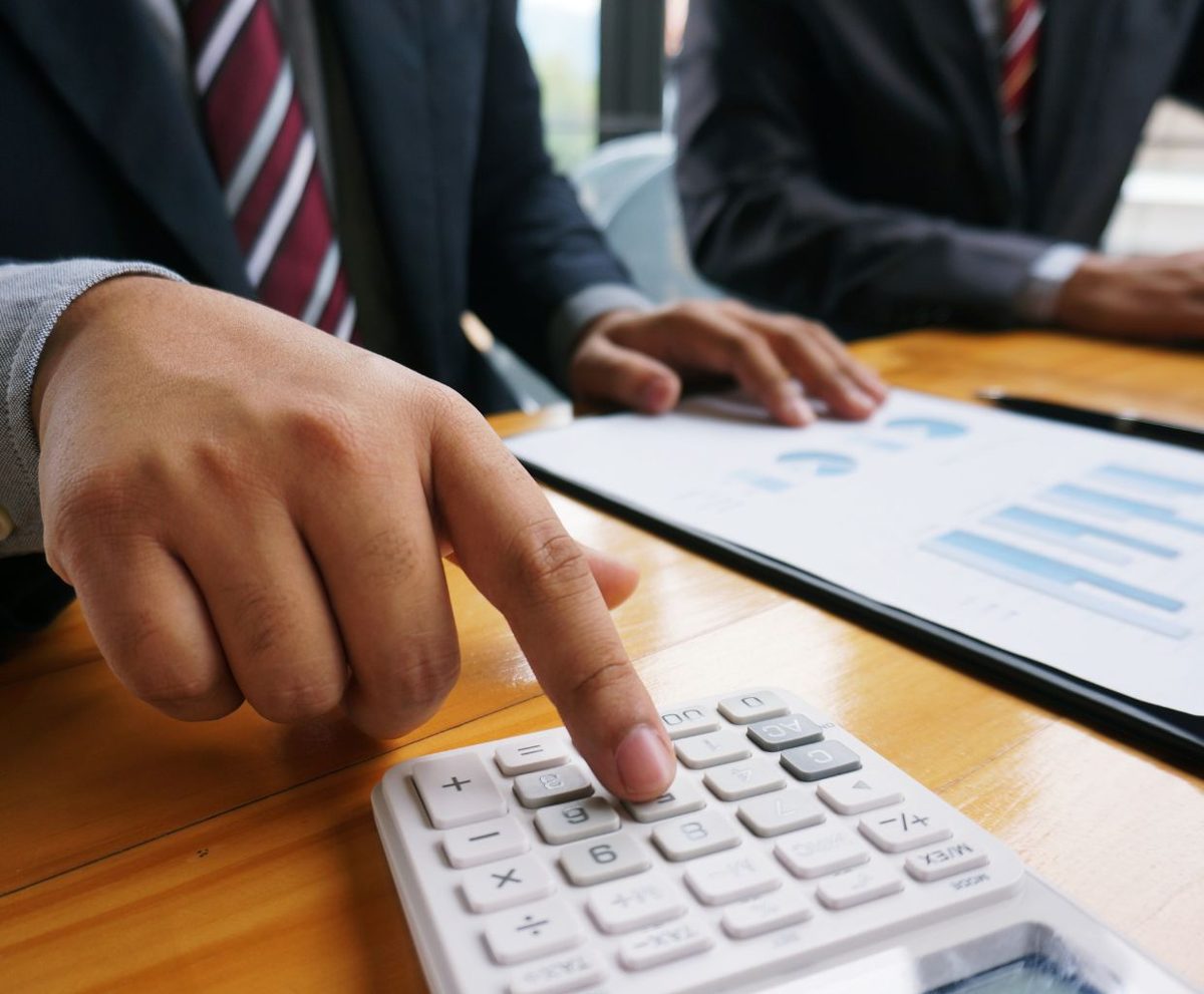 Mano sobre el teclado de una calculadora junto a papeles en una mesa