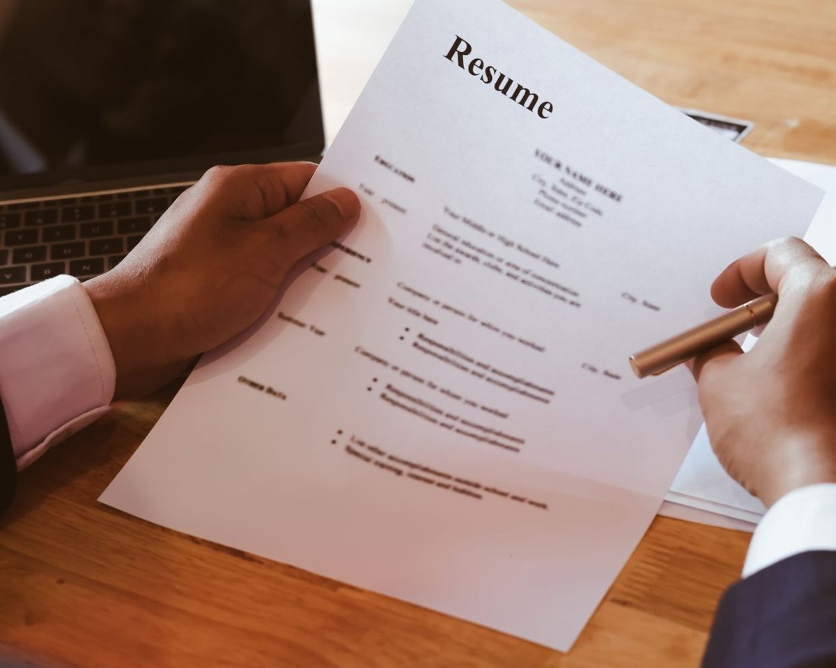 Manos sosteniendo un currículum impreso con la palabra Resume sobre una mesa de madera