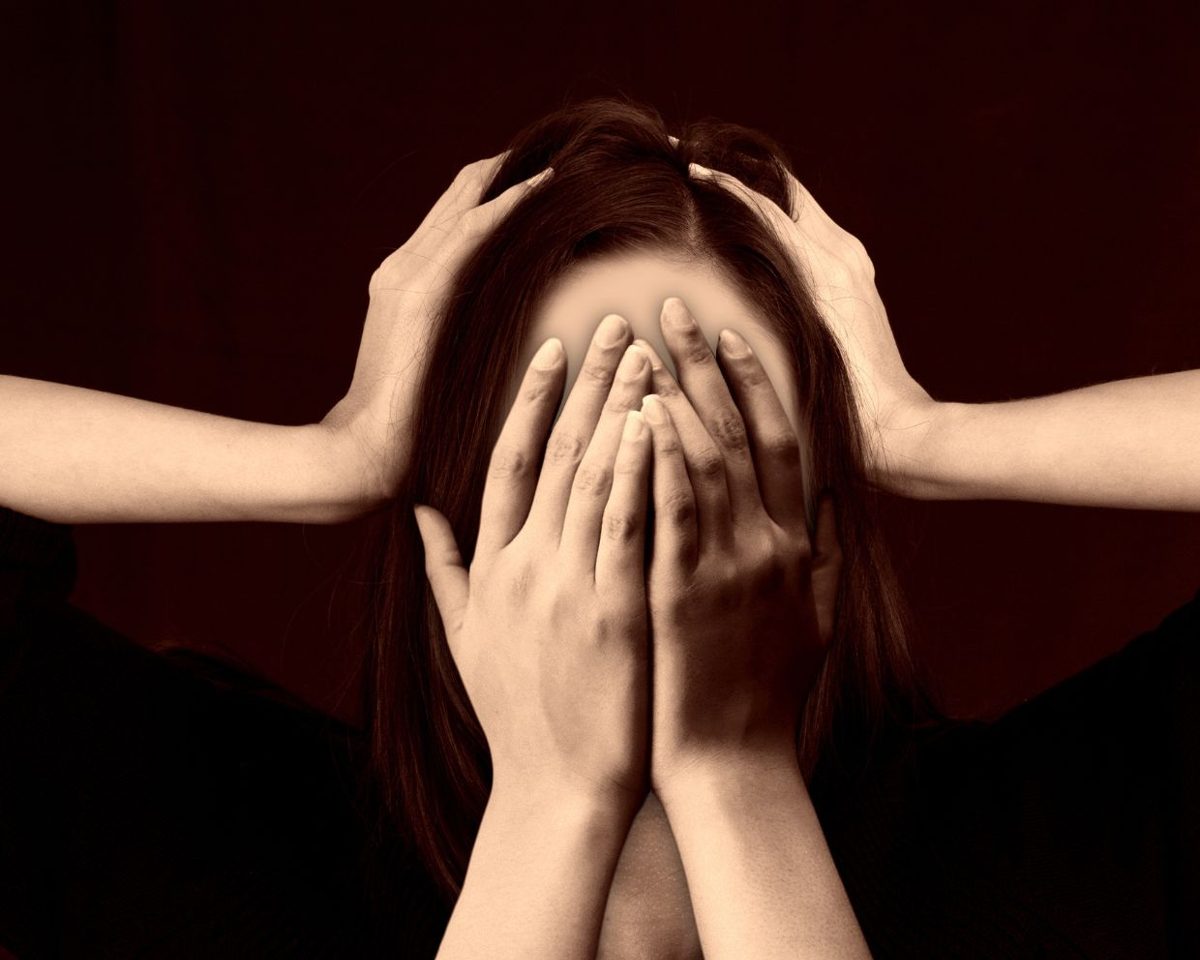 Mujer con las manos cubriéndole la cara sobre un fondo oscuro con manos que le sujetan la cabeza