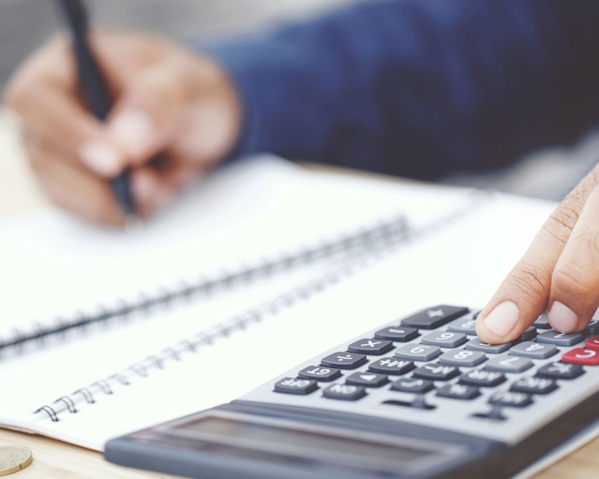 Mano con un bolígrafo junto a una calculadora y un cuaderno sobre una mesa
