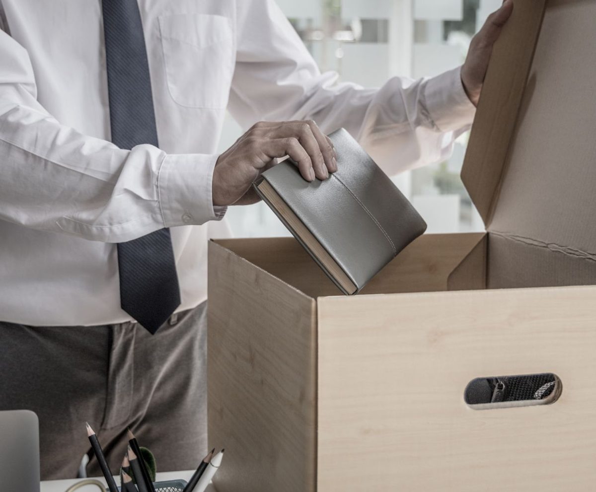 Persona con camisa y corbata guardando objetos de su escritorio en una caja de cartón