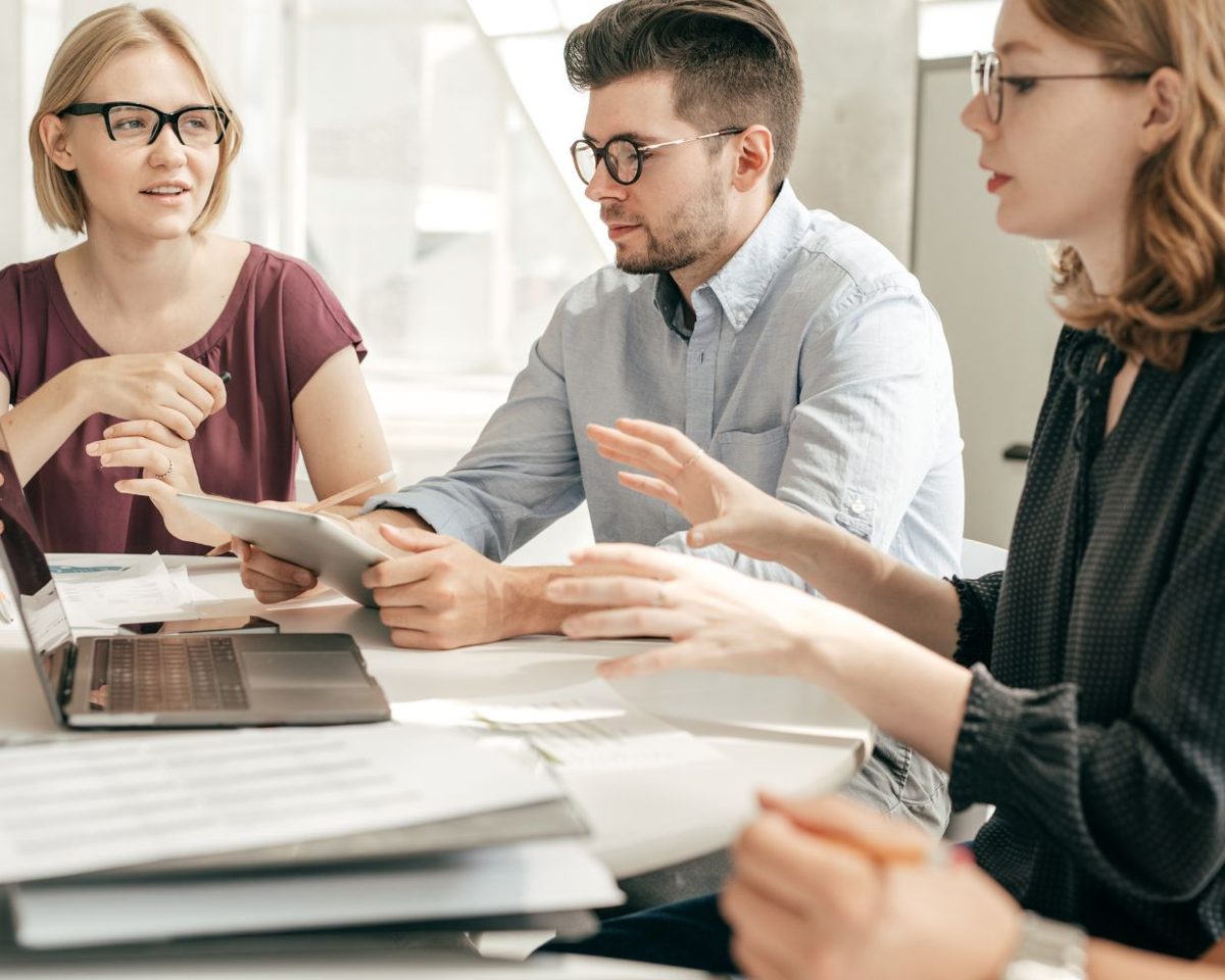 Tres personas de un equipo conversando alrededor de una mesa con portátiles y documentos