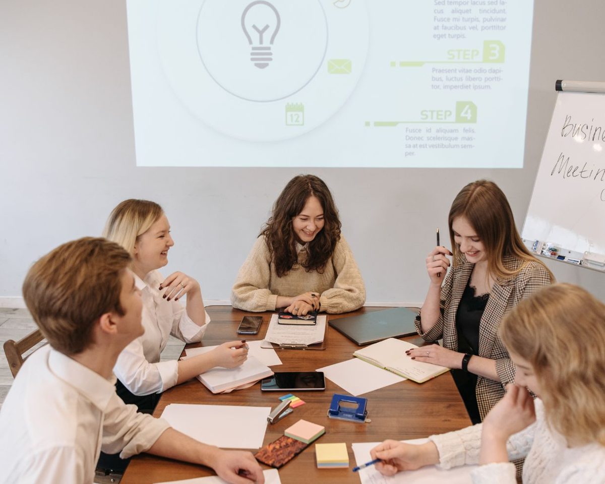 Grupo de personas sentadas alrededor de una mesa de reuniones con una presentación sobre ideas en la pantalla