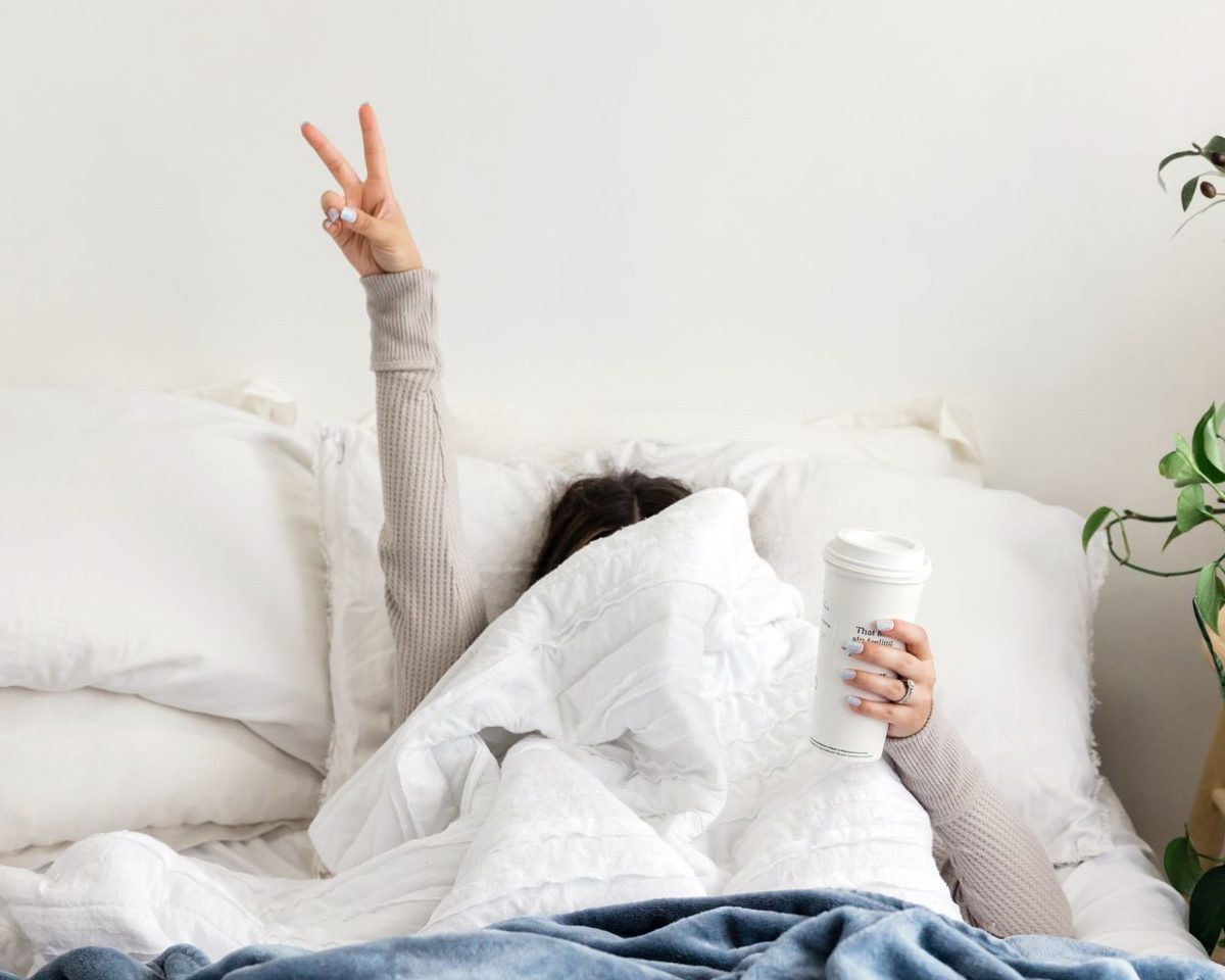 Mujer tumbada en la cama con las sábanas blancas estirando un brazo con la mano en gesto de victoria