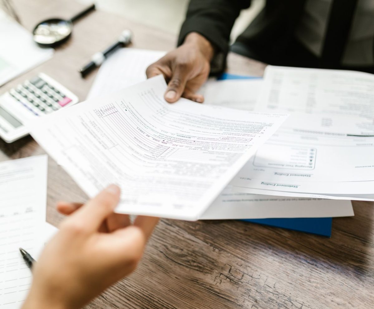 Dos personas se pasan documentos sobre una mesa con una calculadora
