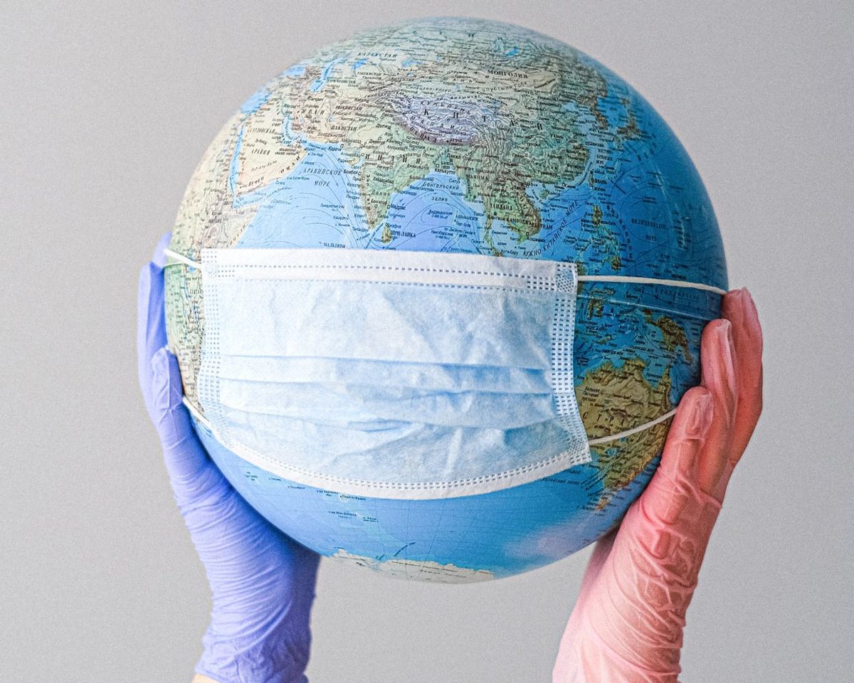 Globo terráqueo sostenido con guantes de látex y cubierto con una mascarilla